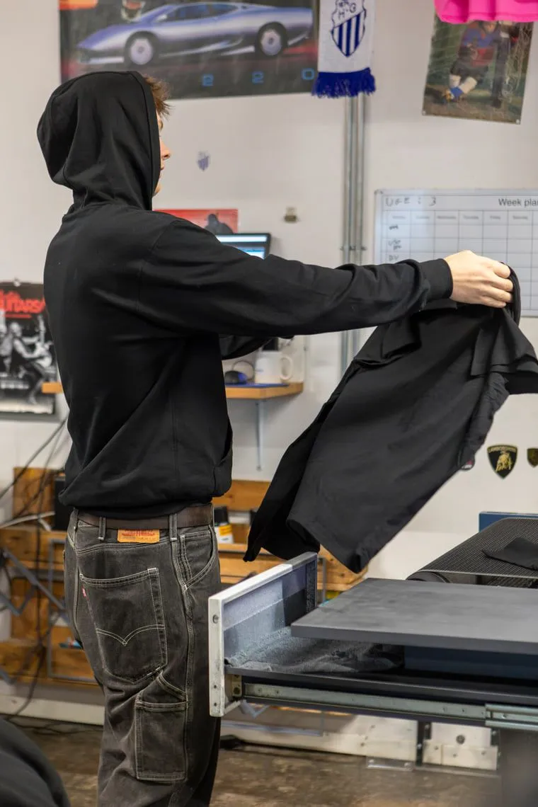 En sort trøje foldet ud i hænderne ved arbejdsbordet.